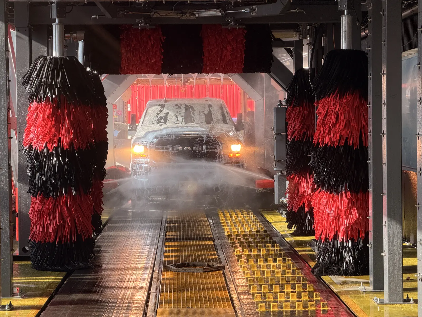 A car on the conveyor between red and black wash brushes