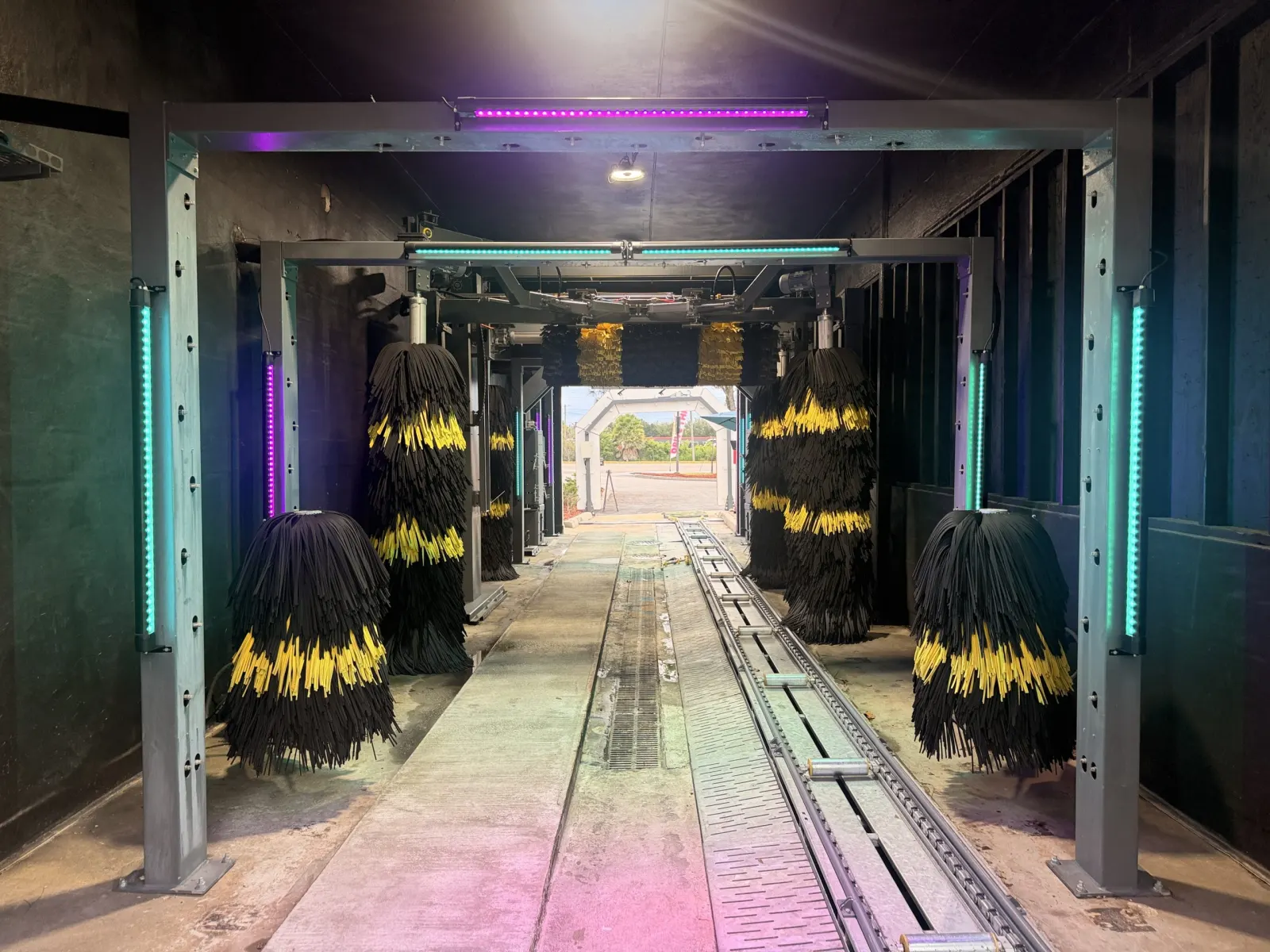 Conveyor lane through lit wash arches with black and yellow brushes