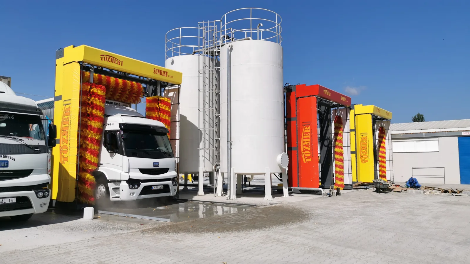 Two SUNRISE W4500 gantries at a depot beside storage silos, a truck in the nearer one