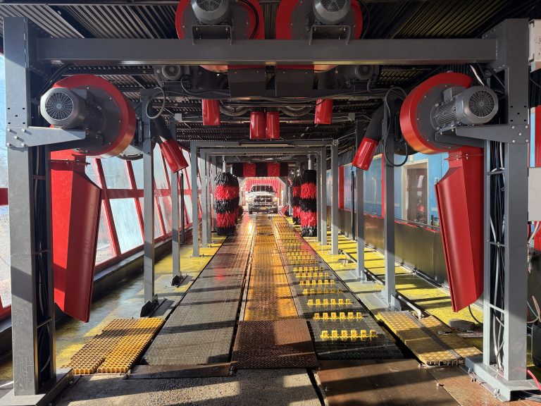 Red dryer blowers, brushes and conveyor guides inside a car wash tunnel.