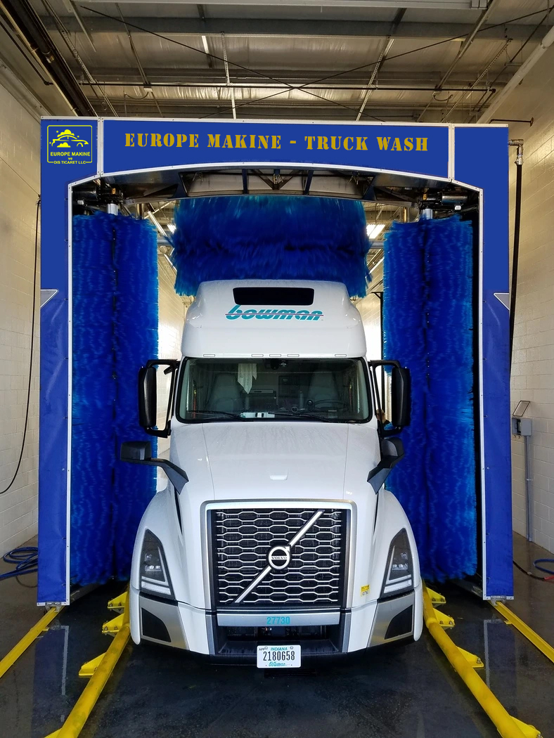 A white truck inside a Europe Makine wash gantry with blue brushes.