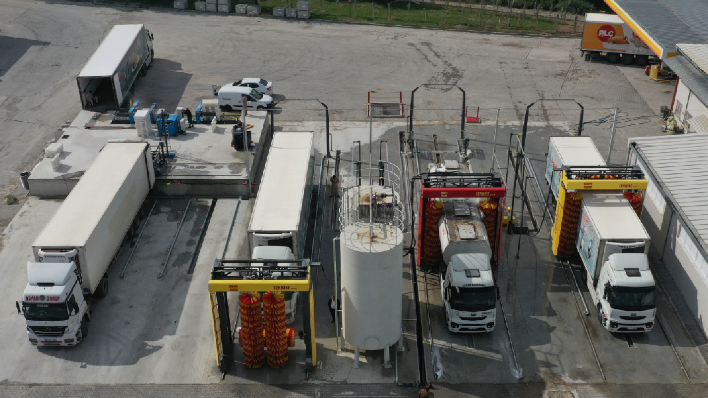 Trucks in parallel outdoor wash bays with brush gantries.