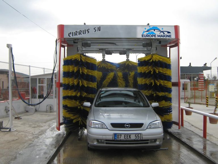 A silver car inside a rollover car wash with blue and yellow side and top brushes.