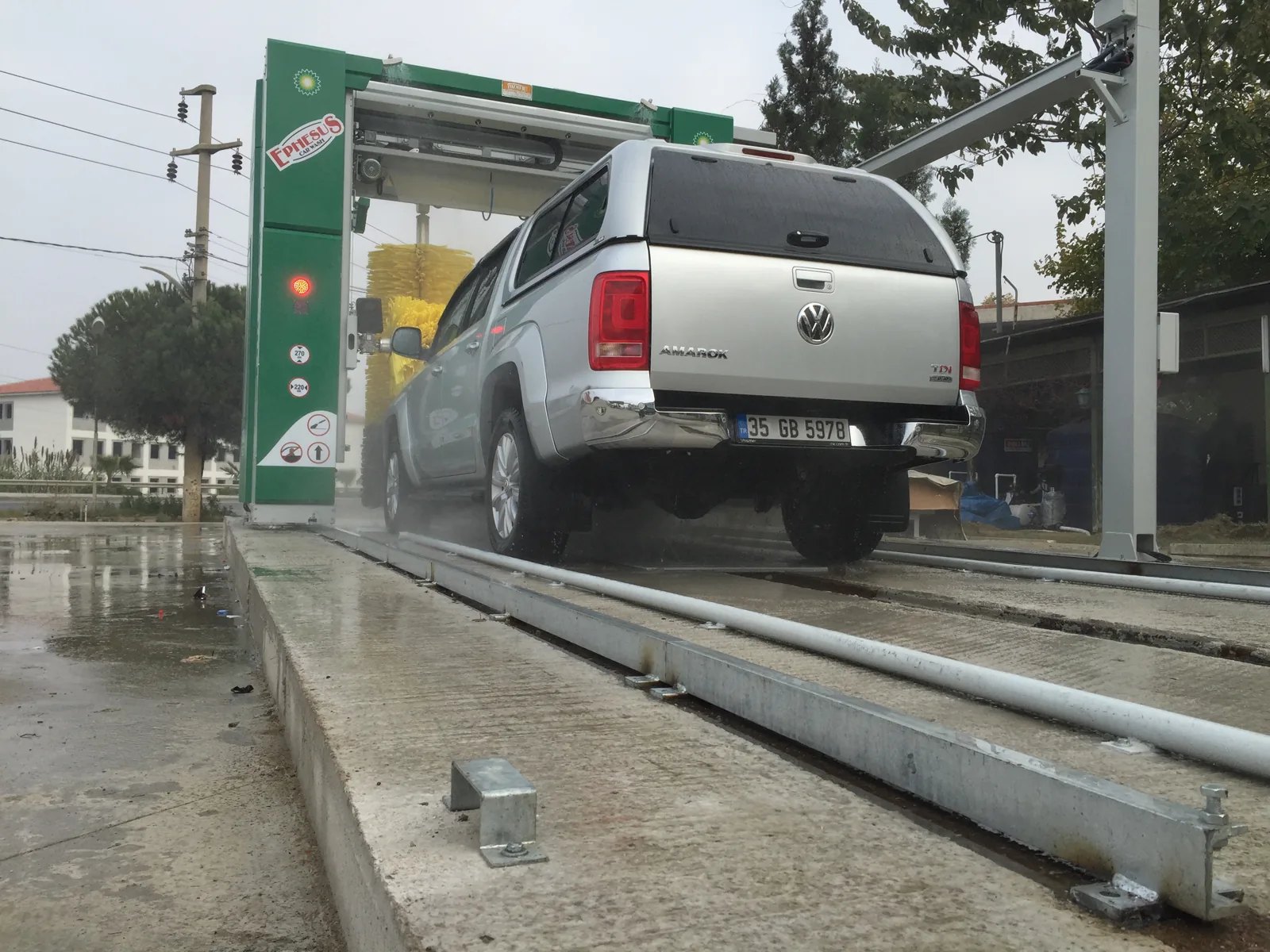 A silver pickup inside a green rollover car wash, seen low along the floor rails.
