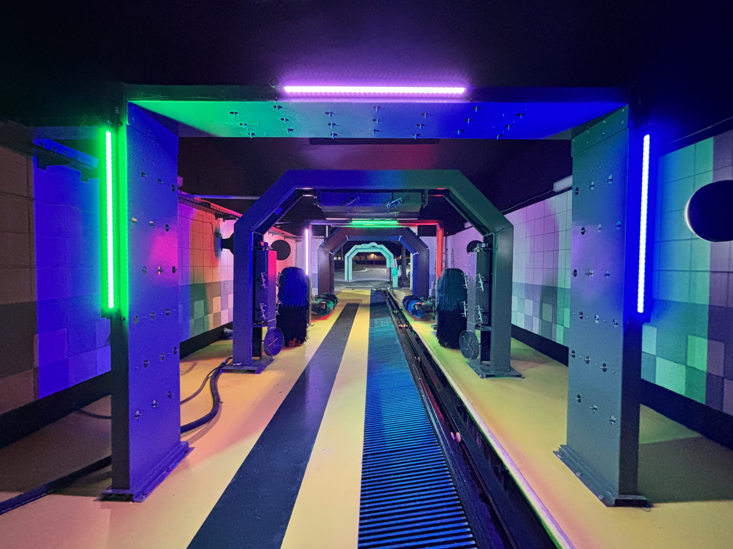 Illuminated wash arches and brushes along a car wash conveyor.